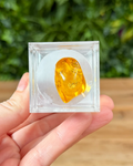 Yellow gemstone in a clear square frame held in a hand with a blurred green background