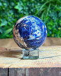 Polished Sodalite sphere in deep navy tones with natural white veining on a white background.