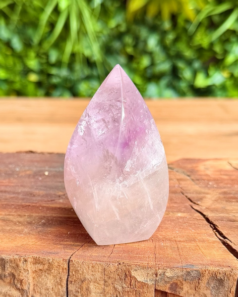 Teardrop-shaped crystal on a wooden surface with a blurred green background