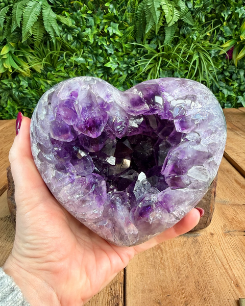 Heart-shaped amethyst geode held by a hand with a natural background