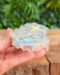 Iridescent shell-shaped object held in a hand with a blurred green background