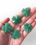 A person holding multiple small green aventurine four leaf clover shaped stones.