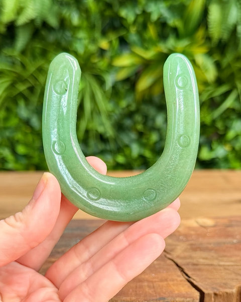 Aventurine horseshoe held by a hand with a blurred green foliage background