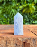 Blue lace agate crystal on a wooden surface with a green leafy background