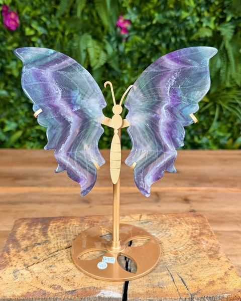 Butterfly-shaped lamp with iridescent wings on a wooden stand against a green foliage background