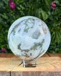 Polished Moss Agate sphere with natural green moss-like inclusions and translucent areas on a white background.