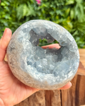Geode crystal held in a hand with a blurred green outdoor background