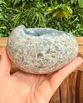 Hand holding a textured stone bowl with greenery in the background