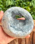 Hand holding a large crystal freeform sphere with a natural background