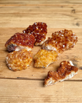 Six pieces of natural crystal jewelry, some orange and some reddish-brown, resting on a light wooden surface.
