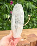 Clear quartz crystal held by a hand with a blurred green outdoor background