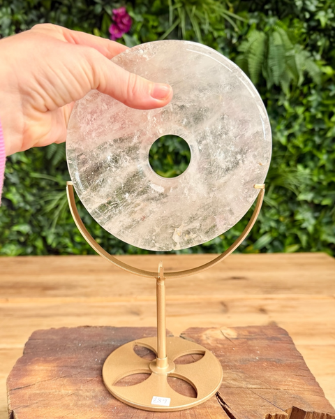 Crystal quartz disc on a gold stand held by a hand with a green leafy background