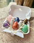 A box designed to look like an egg with six different colorful crystal eggs inside, placed on a wooden surface.