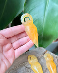 An orange calcite crystal in the shape of a spiral goddess, held in a person's hand.