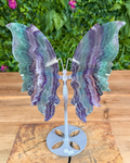 Decorative butterfly with iridescent wings on a wooden surface with greenery in the background
