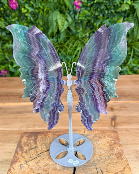Decorative butterfly with iridescent wings on a wooden surface with greenery in the background