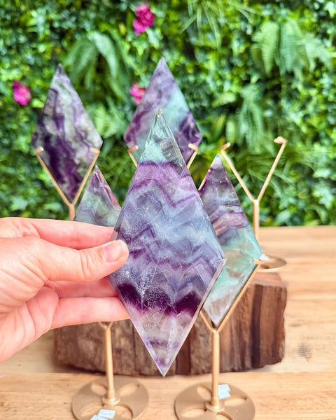 Hand holding a purple and green crystal diamond with a blurred green foliage background