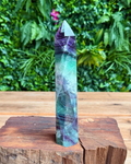 Multicolored crystal tower on a wooden surface with a green leafy background