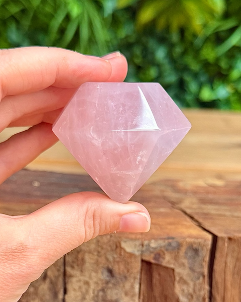 Hand holding a pink rose quartz  crystal against a natural background
