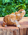 Carved golden healer quartz  elephant on a wooden surface with green foliage in the background