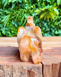 Crystal golden healer quartz elephant figurine on a wooden surface with green foliage in the background