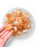 A hand holding a honey calcite tumble stone