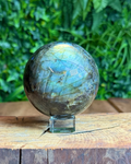 Labradorite sphere with natural iridescent flashes sitting on a display surface, showing its intuitive and protective energy.