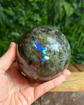 Labradorite sphere with natural iridescent flashes sitting on a display surface, showing its intuitive and protective energy.