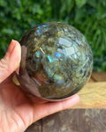 Labradorite sphere with natural iridescent flashes sitting on a display surface, showing its intuitive and protective energy.