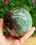 Labradorite sphere with natural iridescent flashes sitting on a display surface, showing its intuitive and protective energy.