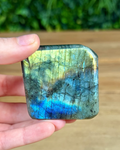 Hand holding a labradorite stone with colorful patterns against a blurred natural background