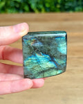 Hand holding a labradorite stone with a blurred green background