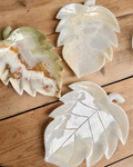Three leaf-shaped white jade plate carvings on a wooden surface