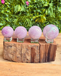Four pink crystal kunzite balls on a wooden stand with a natural background