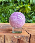 Pink crystal sphere on a wooden surface with green foliage in the background