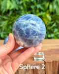 Hand holding a blue kyanite crystal sphere with a blurred green background