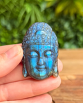 Blue labradorite stone Buddha head held in a hand with a blurred green plant background