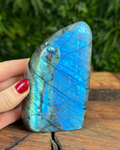 Blue labradorite stone held by a hand on a wooden surface with a blurred green background