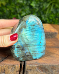 Hand holding a labradorite stone on a wooden surface with greenery in the background
