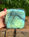 Labradorite stone held by a hand on a wooden surface with greenery in the background