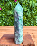 Green crystal tower on a wooden stand with a blurred green foliage background