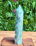 Green crystal obelisk on a wooden stand with a green leafy background