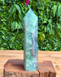 Green crystal tower on a wooden stand with a green leafy background