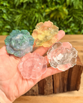 Four colorful lotus flower crystals held in a hand with a natural background