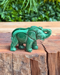 Green malachite elephant figurine on a wooden surface with a blurred green leafy background