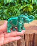 Green crystal malachite elephant figurine held in a hand with a blurred green foliage background