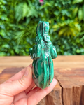 Green malachite crystal held in a hand with a blurred green foliage background