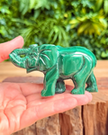 Green malachite elephant figurine held in a hand with a natural background