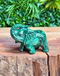 Green malachite elephant figurine on a wooden surface with a blurred green foliage background