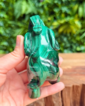 Green malachite elephant sculpture held in a hand with a blurred green foliage background